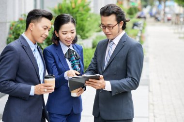 Resmi olarak kahve içen ve şehirde ayakta dururken dijital tablette online sohbet eden iş adamları