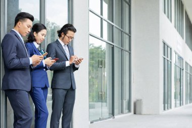 Ofis binasının yanında dururken birlikte cep telefonlarını kullanarak resmi giyim Asyalı iş adamları Grubu