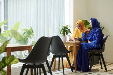 Geleneksel Müslüman elbiseli pozitif genç Müslüman kadınlar toplantıda masa ekranında bilgi tartışıyor