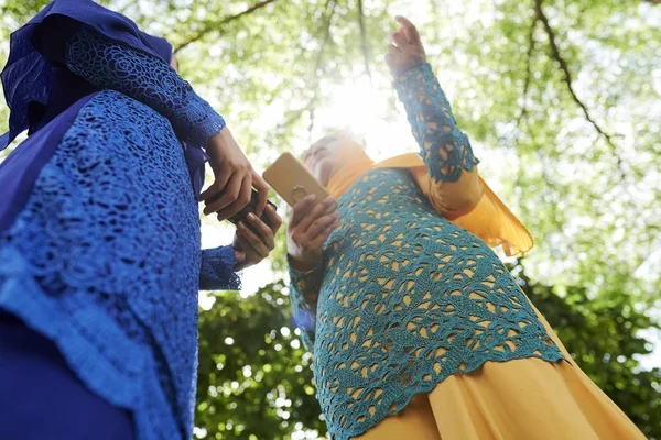 身着穆斯林服装的妇女站在公园里用智能手机和讨论新闻 从下面看 — 图库照片