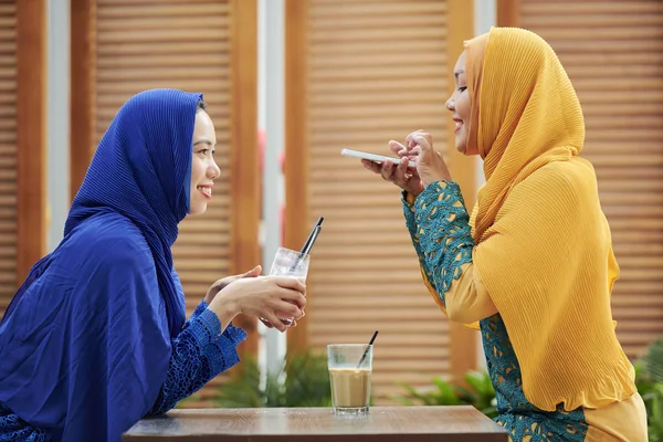 Creative young woman in hijab taking photo of her friend with tasty refreshing cocktail