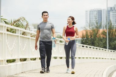 Fit sabah çalıştırdıktan sonra su şişeleri ile köprüüzerinde yürüyen Asyalı erkek ve kadın gülümseyen