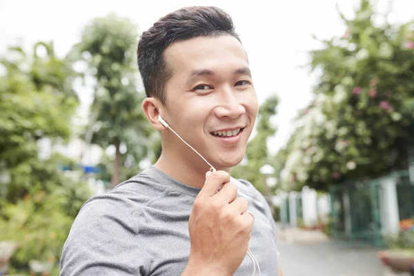 彼の耳のトレーニング屋外でイヤホンを持つ陽気なアジアのスポーツマンの肖像画 — ストック写真