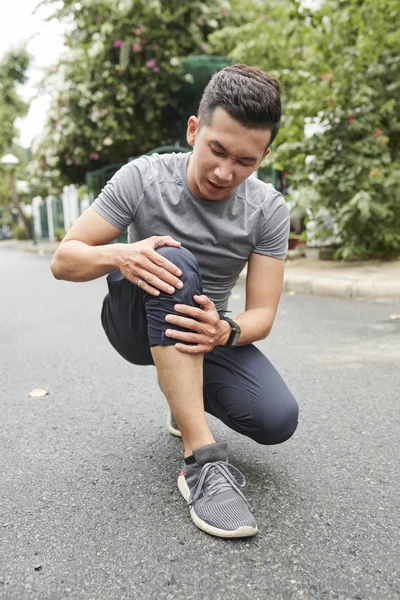 若いアジアのスポーツマンは 屋外で走っているときに彼の膝を痛めた — ストック写真