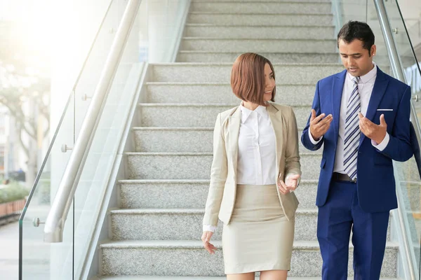 Business couple walking down the stairs of modern office and discussing their working moments together