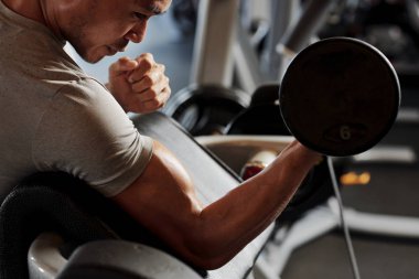 Yakın çekim Asyalı genç vücut geliştirmeci oturma ve spor salonunda dumbbell ile egzersiz yapıyor