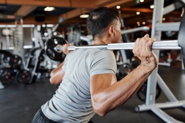 Omuzlarında halter ve spor salonunda eğitim ile ayakta genç atlet arka görünümü