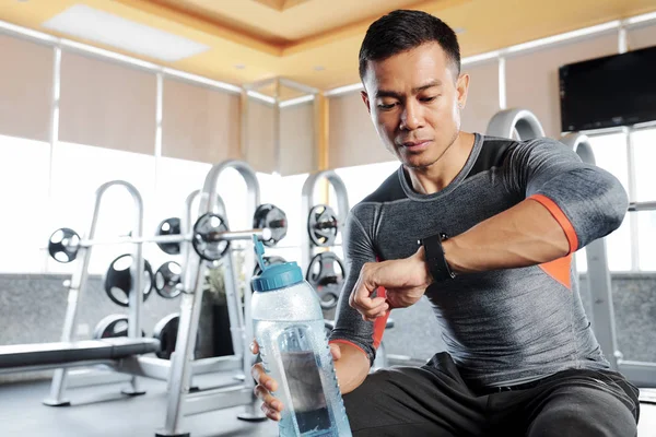 年轻的英俊的亚洲健身男子检查智能手表后 在健身房的高强度训练 — 图库照片