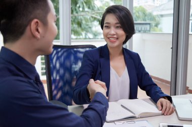 Asyalı genç iş kadını eşine el sıkışma ve ofiste iş toplantısı sırasında gülümseyerek