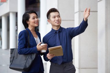 Asyalı genç işadamı bina işaret ve onlar açık havada ayakta iken gülümseyen iş kadını için yol gösteren