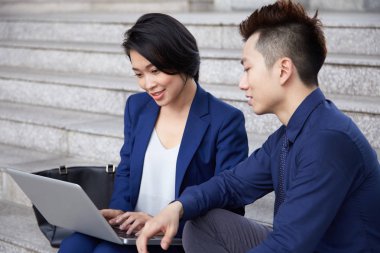 Asyalı iş adamları şehirde merdivenlerde oturan ve dizüstü bilgisayar kullanarak takım birlikte online çalışma