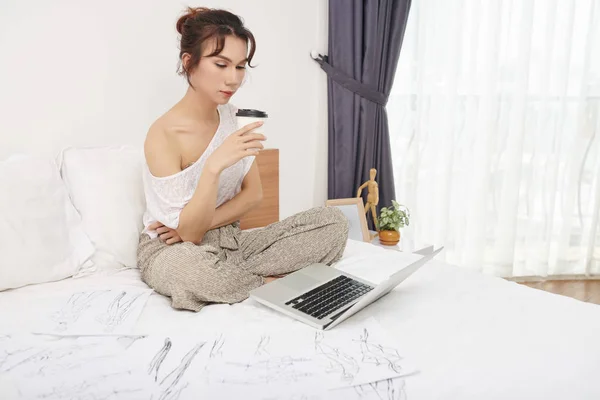 Seriöse Designerin Sitzt Mit Kleidungsskizzen Auf Dem Bett Blickt Auf — Stockfoto