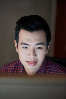 Pozitif Vietnamlı adam gece çalışırken bilgisayar ekranında bilgi okuma