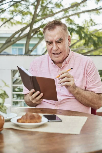 Senior man having breakfast in cafe writing plans for the week in his planner