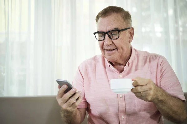 正老男子在眼镜喝卡布奇诺杯和阅读短信在他的手机 — 图库照片