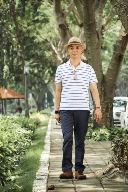 Asyalı yaşlı adam yeşil ağaçların sokak boyunca tek başına yürüyüş ve yaz günü açık havada onun yürüyüş zevk
