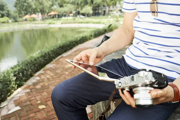 デジタルカメラを持って座り 公園内のデジタルタブレットのディスプレイを見ているシニア男性のクローズアップ — ストック写真