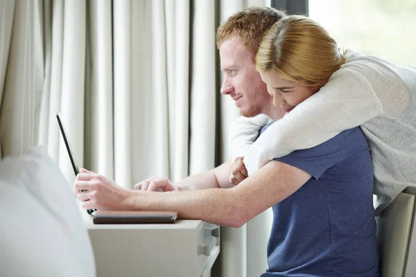 漂亮的女人拥抱她的男朋友从后面时 他正在笔记本电脑上工作 — 图库照片