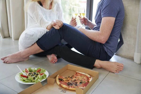 Young couple sitting on the floor with pizza and salad, drinking wine and talking