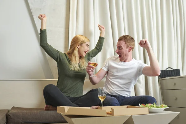 Happy excited couple with glass of wine celebrating victory of favorite team