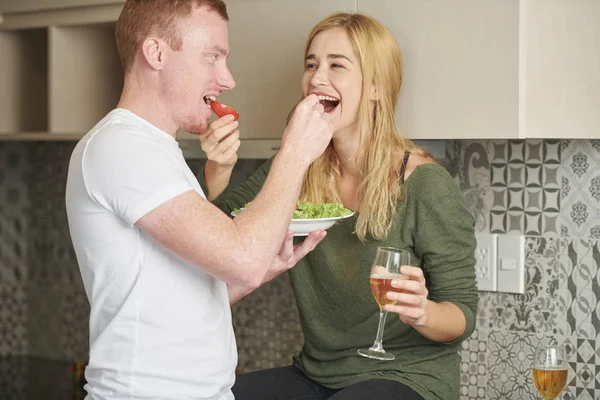 Happy young boyfriend and girlfriend feeding each other when having romantic dinner at home