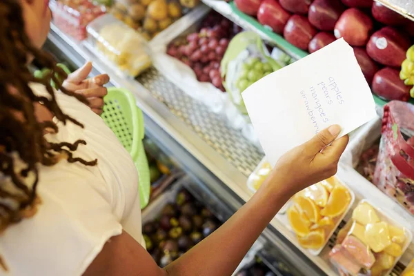 スーパーで果物やベリーを買うときに買い物リストをフォローする女性客 — ストック写真