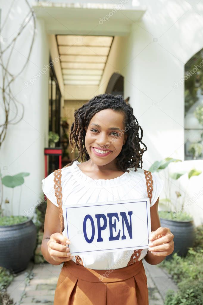 Portrait of positive excited young Black woman holding open sign