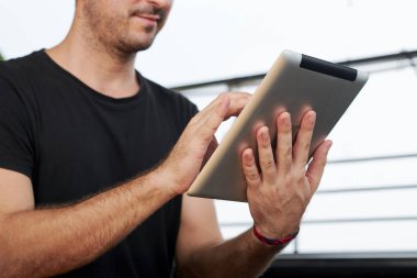 Kafede otururken dijital tablet tutan ve iletişim kuran ya da çevrimiçi çalışan genç adamın yakın çekim