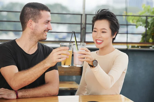 幸せな若いカップルは テーブルに座って カフェでの会議中に新鮮なジュースのグラスで乾杯 — ストック写真
