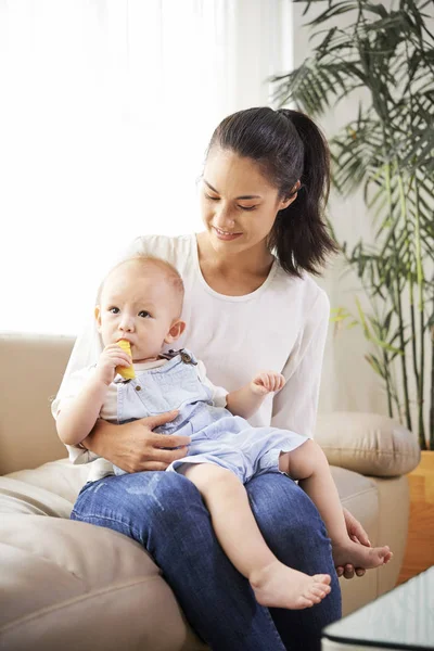 Mujer Joven Sonriente Sentada Sofá Con Bebé Masticando Rebanada Manzana —  Fotos de Stock