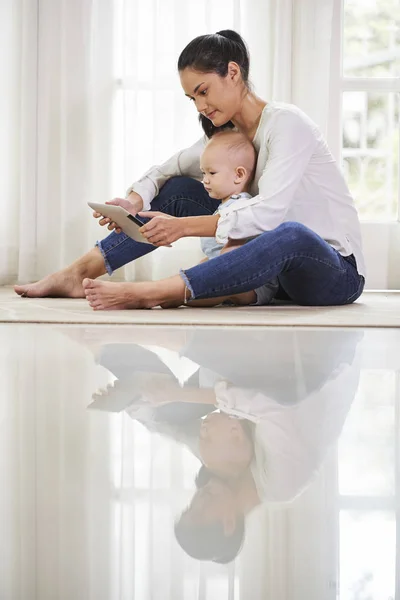 Mother and child watching cartoon on tablet computer reflecting in glossy floor surface