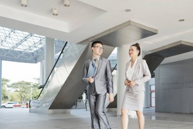 Asya iş ortakları birbirleriyle konuşurken ve modern ofis boyunca giderken gülümseyerek