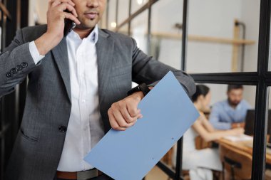 Takım elbiseli işadamının yakın çekim cep telefonuyla konuşuyor ve kol saatinde zamana bakıyor ve acele ediyor