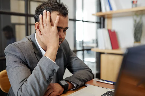 Exhausted office worker sitting at the table with laptop computer at office and suffer from headache