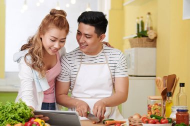 Güzel genç Asyalı kadın onu pişirme kocasına tarifi ile tablet bilgisayar gösteren