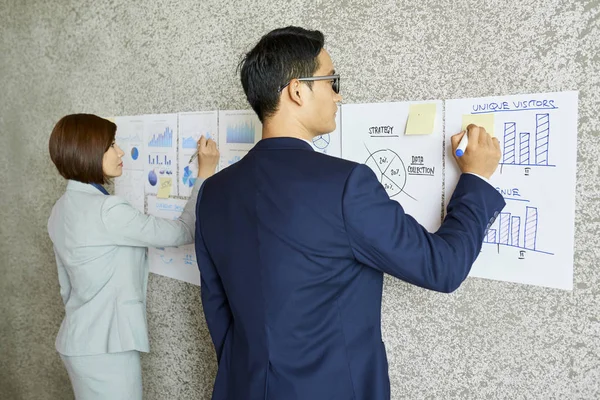 ベトナムのビジネスマンは オフィスの壁に掛かっているチャートや図にメモを取る — ストック写真