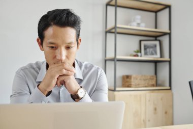 Pensive genç Asyalı işadamı dizüstü bilgisayar ekranında e-postaları okuma