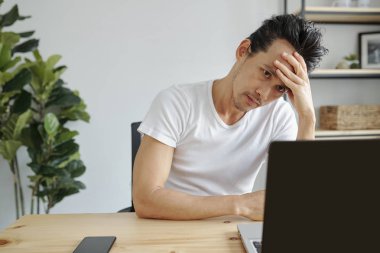 Ofis masasında dizüstü bilgisayar üzerinde çalışan sıkılmış veya stresli Asyalı adam Portresi