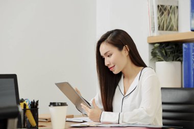 Asyalı genç yönetici ofiste ki işyerinde dijital tablet üzerinde online çalışıyor