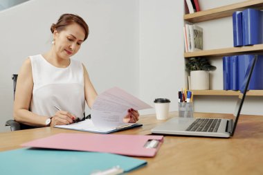 İşyerinde dizüstü bilgisayar ve belgeyi okuyup imzaladığı belgelerle çalışan kadın yönetici