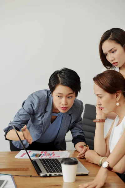 亚洲年轻女商人指着笔记本电脑 向女领导展示在线项目 而她坐在桌旁 仔细看着它 — 图库照片