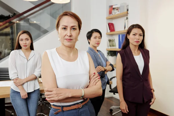 腕を組んで立っている自信に満ちた女性リーダーの肖像画と オフィスの背景にある彼女のチームとカメラを見る — ストック写真