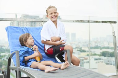 Portakal suyu ile birlikte şezlong üzerinde otururken kamera gülümseyen mutlu çocuk Portresi açık havada