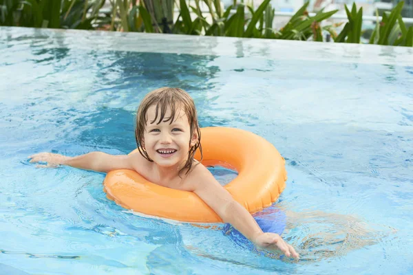 屋外のプールでオレンジ色のライフリングで泳ぐことを学び カメラで微笑む幸せな小さな男の子の肖像画 — ストック写真