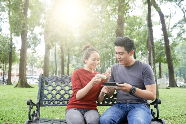 年轻的越南夫妇坐在长椅上 在公园里吃春卷 — 图库照片