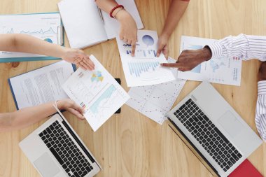 Dizüstü bilgisayarlarla tahta masada oturan ve finansal grafikler ve grafiklerle farklı raporları işaret eden iş adamlarının yakın çekim