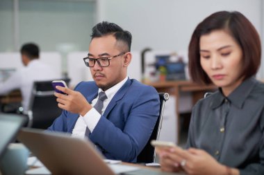 Asyalı iş adamları oturma ve ofiste bir iş toplantısı sırasında cep telefonlarını kullanarak