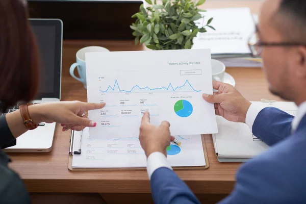 財務グラフとチャートを含む文書を指し 進捗状況を議論するテーブルに座っているビジネスパートナーの背面図 — ストック写真