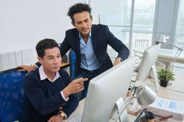 Modern ofiste birlikte çalışırken finansal verilerle bilgisayar monitörü bakarak iki Asyalı erkek