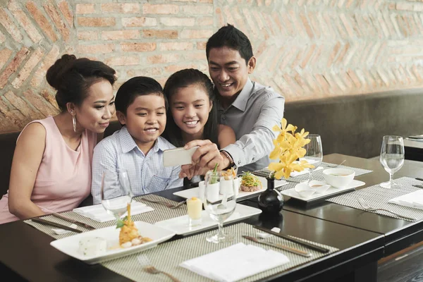 レストランで注文を待っている間にスマートフォンで自分撮りポートレートを作る4人の幸せな家族 — ストック写真